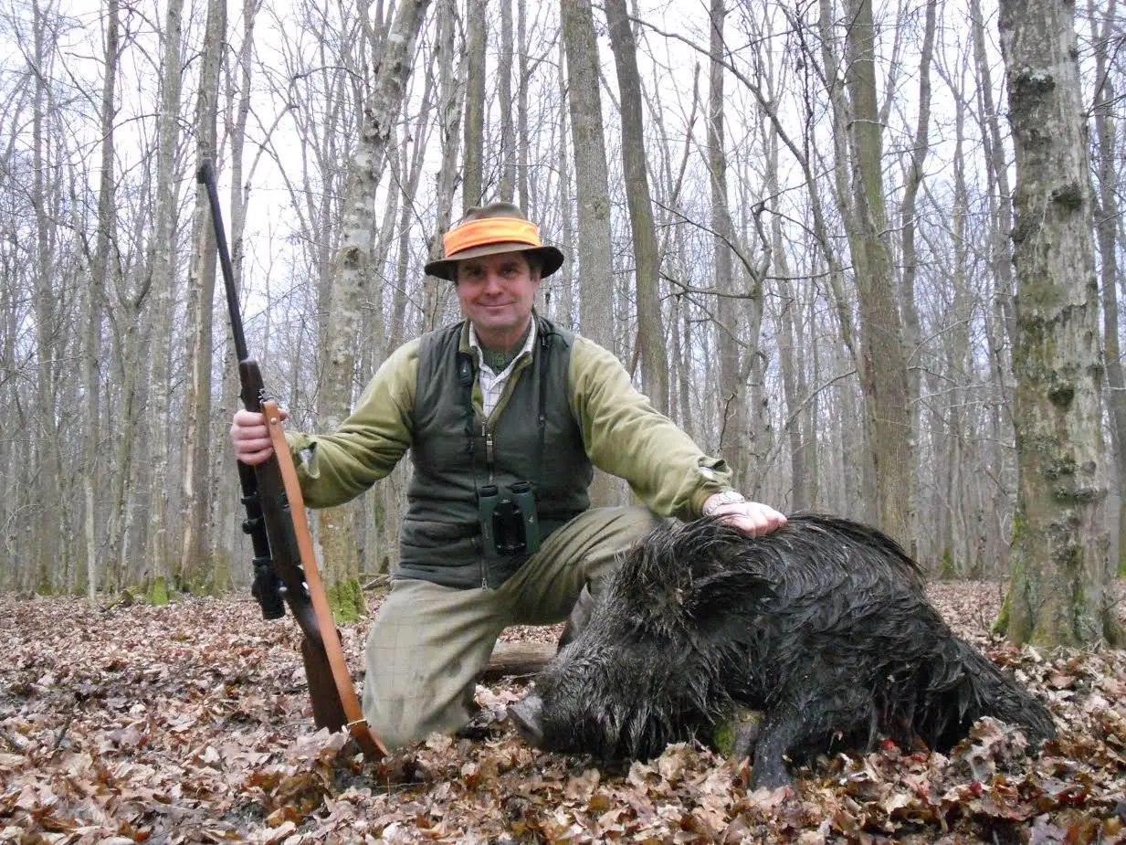 A hunter kneeling beside a wild boar in a leafy oak forest